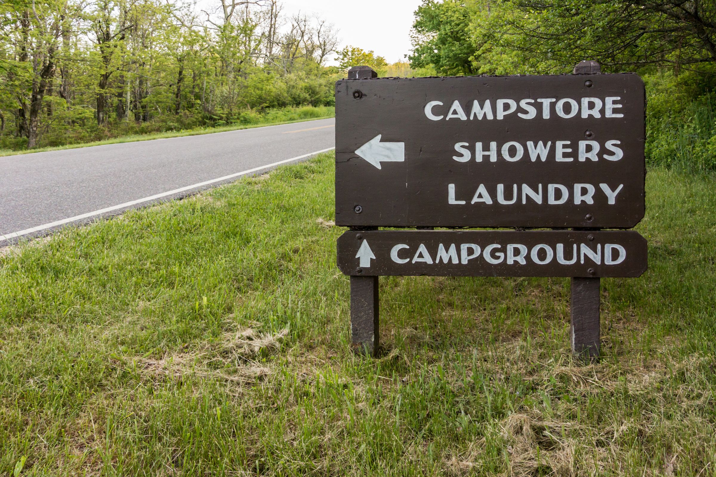 ExploreGear.com | Wooden campground sign with directions to campstore, showers, laundry, and campground, surrounded by greenery.