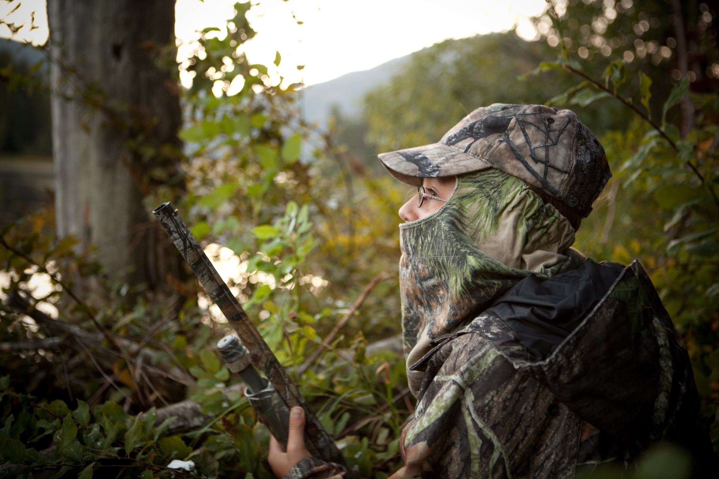 ExploreGear.com | Hunter wearing camouflage gear holding a shotgun in dense foliage.