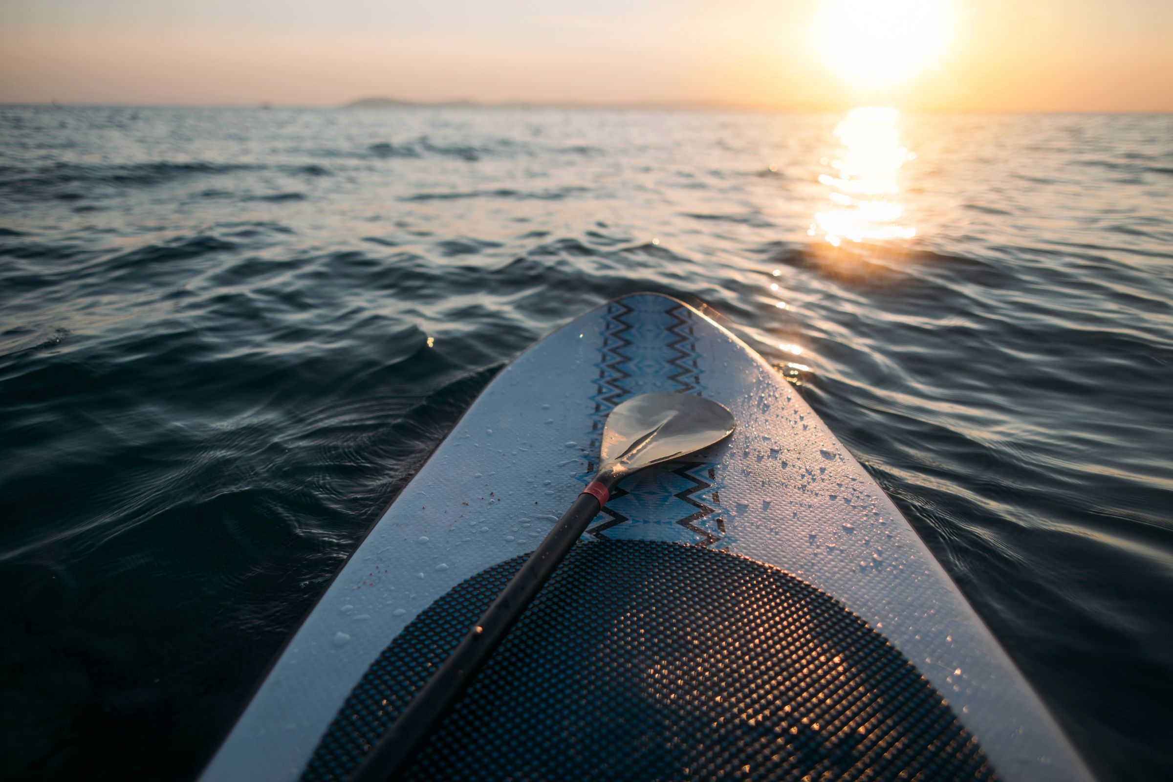 ExploreGear.com | Paddleboard with paddle on calm water at sunset.