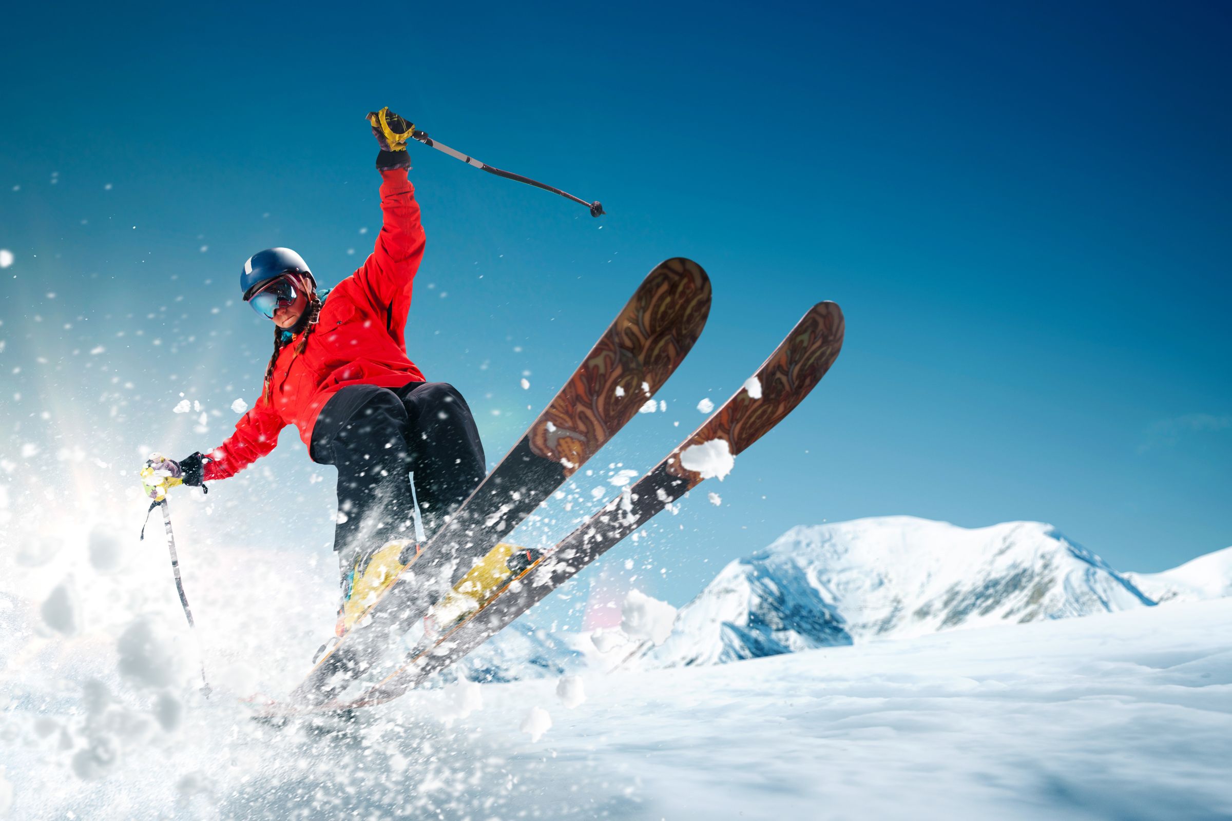 ExploreGear.com | Skier jumping snow-covered slope with bright blue sky.